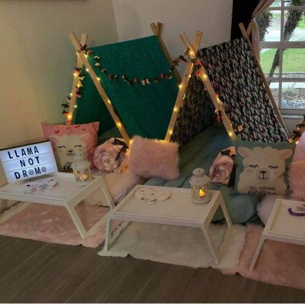 Cozy teepee setup for children with lights, cushions, and small tables, featuring a decor with cute animal designs and playful text.