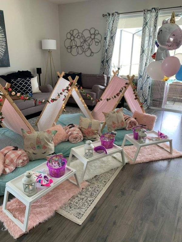 Indoor children's party setup with small teepee tents, cushions, and a picnic arrangement with table settings and decorations in a Lakeland-inspired living room transformed into a cozy glamping haven, featuring teepees adorned with vibrant balloons.