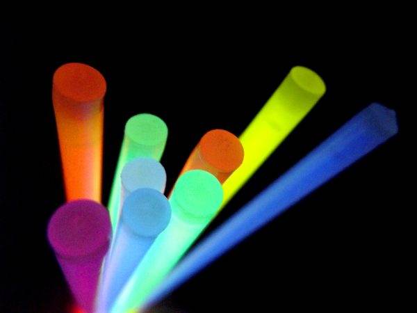 Colorful neon glow sticks in various colors such as orange, yellow, green, and blue lit up in a dark setting, fanning out from a central point.