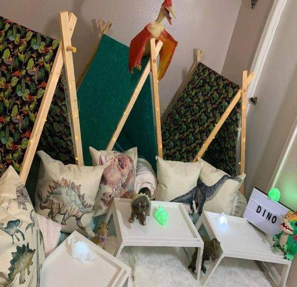 A child's play area with dinosaur-themed pillows, toys, and home decor, including easels and a "dino" sign.