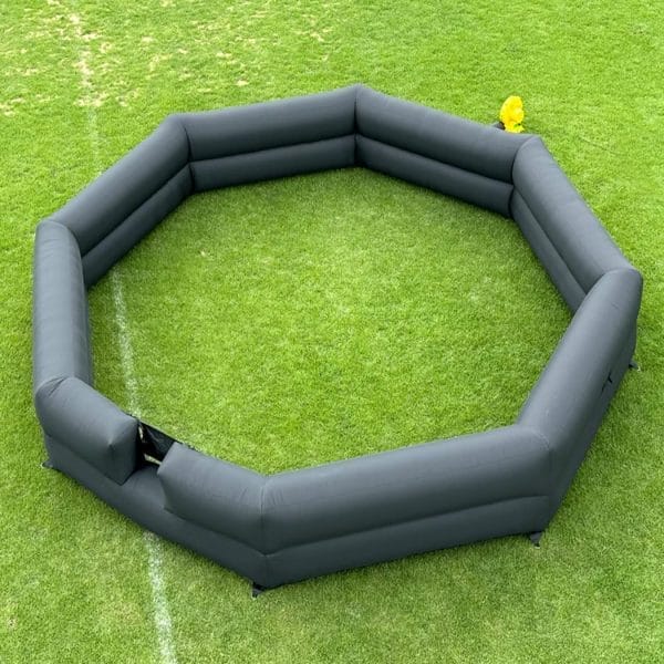 Inflatable black octagonal barrier on green artificial turf with a small yellow ball inside, available as a Foam Machine Rental Addon.