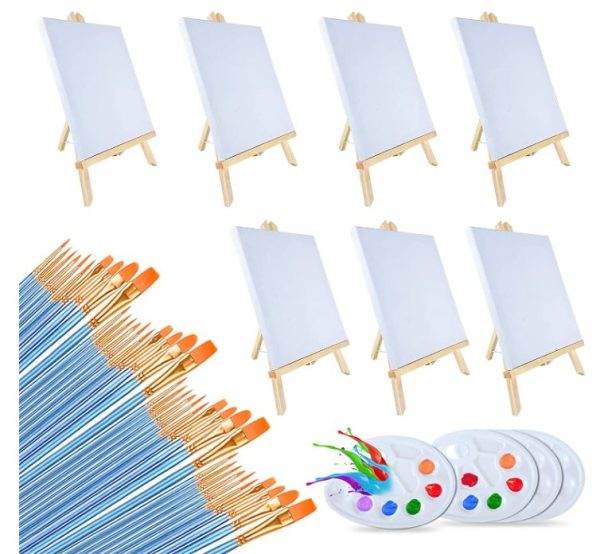 Six small easels each displaying a blank canvas, arranged in two rows of three, with a scattered array of paintbrushes and a Color Pops Painting Party Kit palette filled with various colors in the foreground.