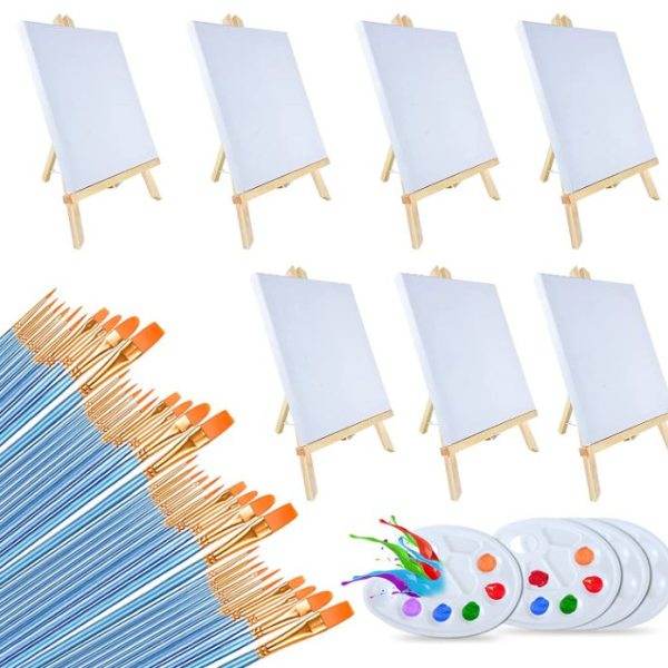 Six small easels each displaying a blank canvas, arranged in two rows of three, with a scattered array of paintbrushes and a Color Pops Painting Party Kit palette filled with various colors in the foreground.