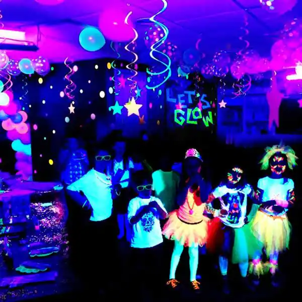 A party in a room with neon lights and balloons of children in neon outfits and glowing accessories, surrounded by colorful decorations and streamers.