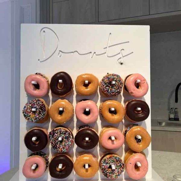 A counter top display spelling "donuts" with a variety of colorful glazed and sprinkled donuts arranged in a grid pattern below it in a modern XL outdoor games setting.