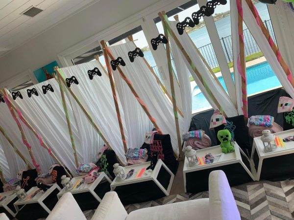 A Gamer Party setup with teepee-style tents adorned with colorful ribbons, plush toys, and bedding inside, all arranged in a room with a pool view.