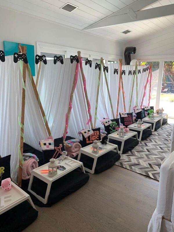 Indoor party setup with sleepover tent rentals, decorated with colorful ribbons and themed cushions, each with a small table set with crafts.