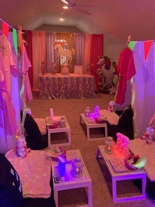 Indoor unicorn-themed party setup with colorful decorations, small tables with cushions, sleepover tent rentals, and inflatable unicorn figures.