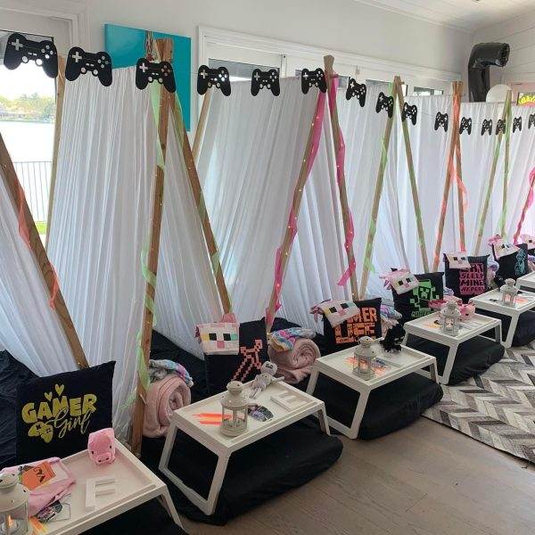 A room set up for a Gamer Teepee Party Theme sleepover with tent rentals, each adorned with colorful ribbons and gaming controllers. The tents have cushions and small tables with gaming props and snacks.