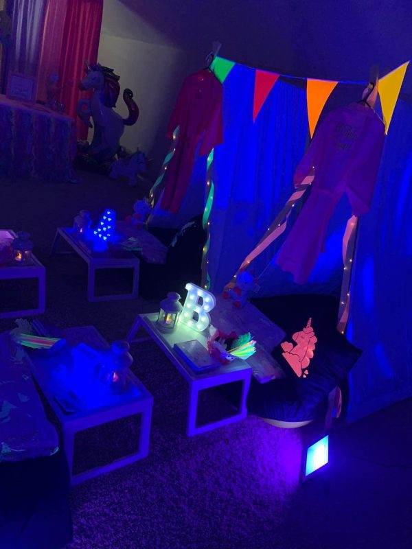 A dimly lit party room with colorful pennant banners and sleepover tent rentals, featuring small tables, cushions, and a floor setup for children.