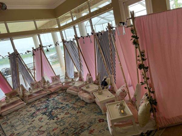 An indoor spa setting with multiple curtain-enclosed massage areas, pink drapes, plush pillows, and floral decorations, overlooking a body of water through large windows featuring the 288176602_1423306754760178_2525960957445769797_n product.