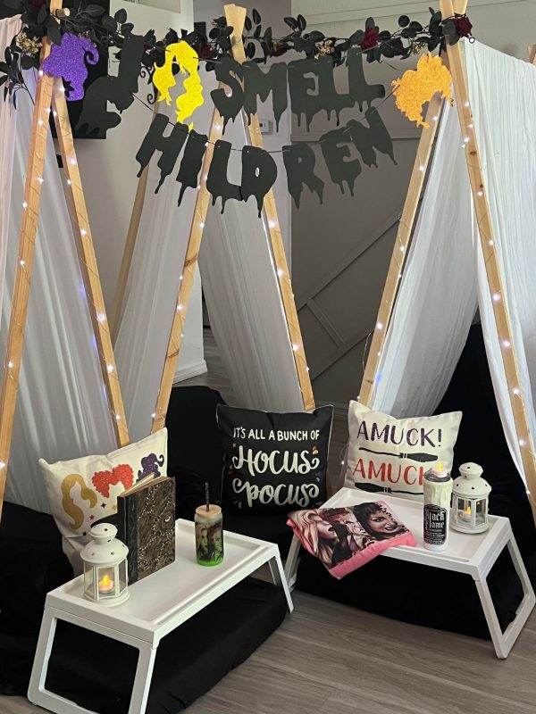 Halloween-themed photo booth with "i smell children" banner, sleepover tent rentals, candles, and movie-themed signs reading "hocus pocus" and "amuck! amuck!