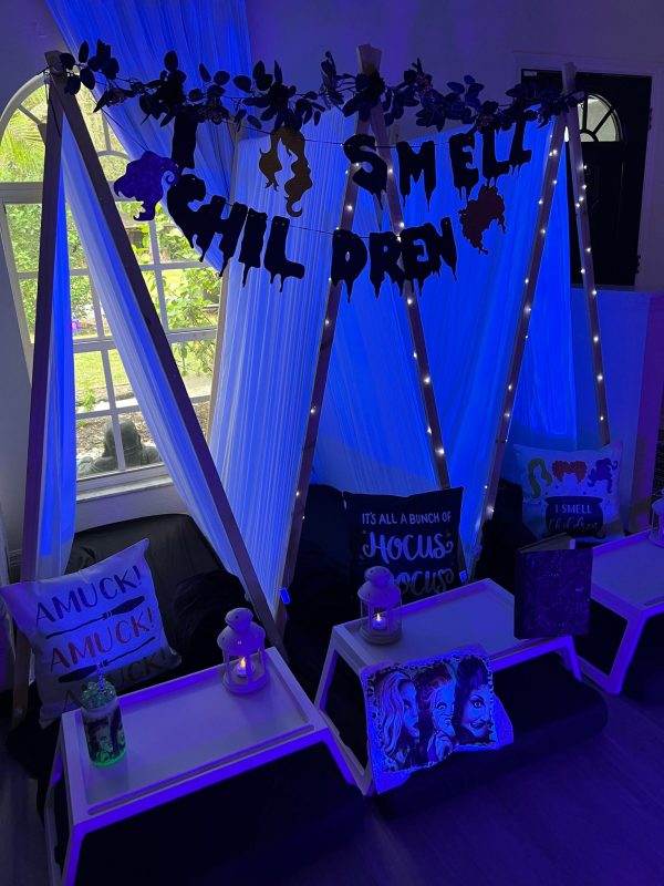 Indoor Halloween-themed sleepover tent rentals with blue lighting, featuring pillows, candles, and silhouettes of witches on the window.