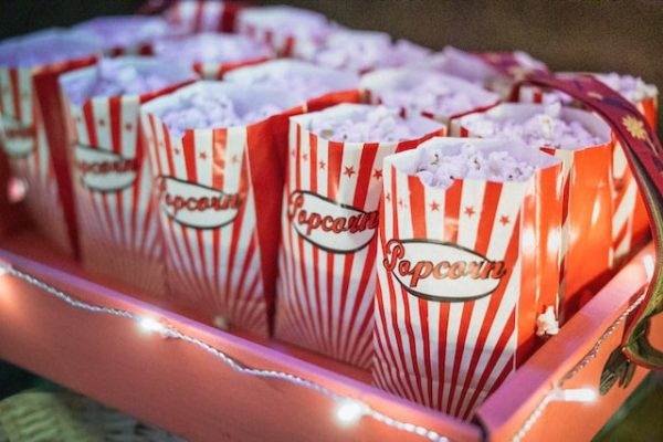 Red and white striped popcorn bags filled with popcorn in a tray illuminated by fairy lights, ready for slumber party activities.