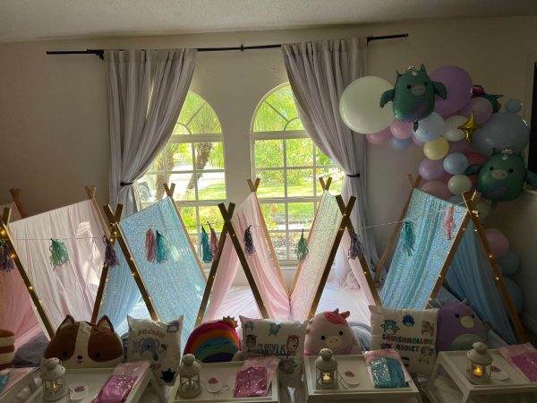 Indoor sleepover party setup with small tent 315526822_670643308023606_7109049524827420248_n draped in pastel fabrics, decorated with balloons and colorful pillows, and equipped with individual trays and lanterns.