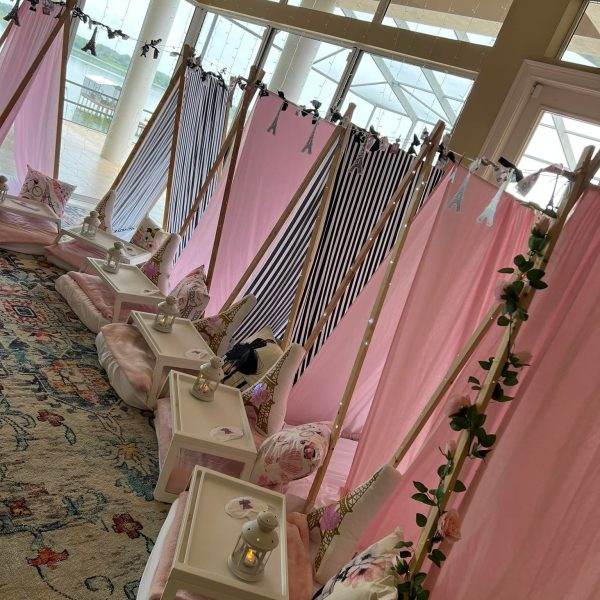 An indoor setup of a beauty spa with multiple pink teepee tents for a girl's birthday party featuring Slime decorations, cushioned seats, and individual mirrors, designed for a unique client experience.