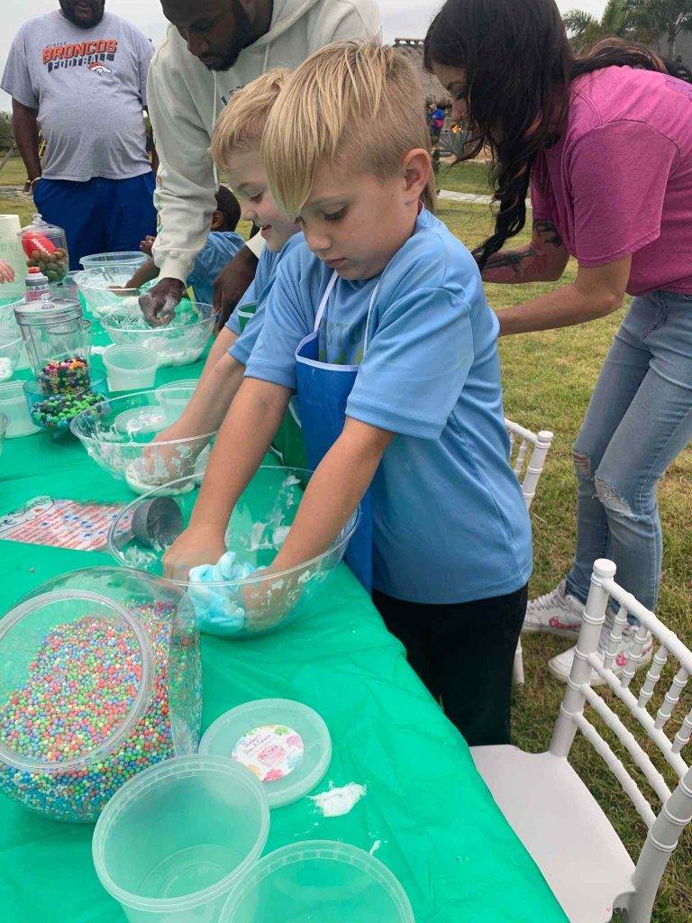 A group of children at a table with a green tablecloth, engaged in a fun activity involving slime.