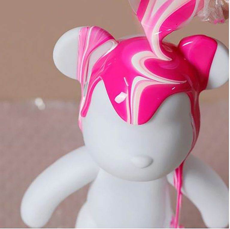 A close-up of a Lakeland teddy bear with a pink and white marbled head being decorated with swirling pink paint at a wedding, perfect for kids' activities.