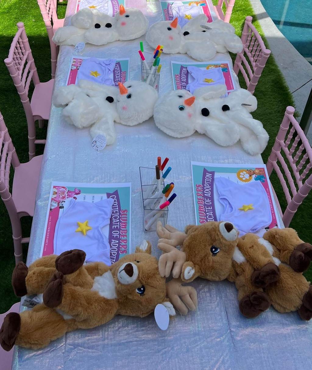 Children's party table set up with stuffed bears, fluffy cloud mats, coloring materials, and kids' activity sheets.