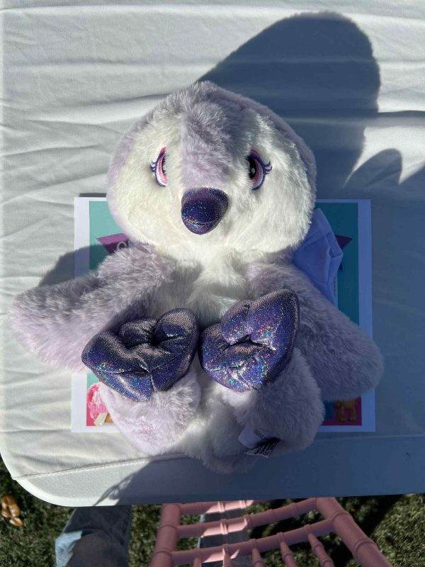 A plush toy penguin with sparkling purple accents sitting on a table at an outdoor party.