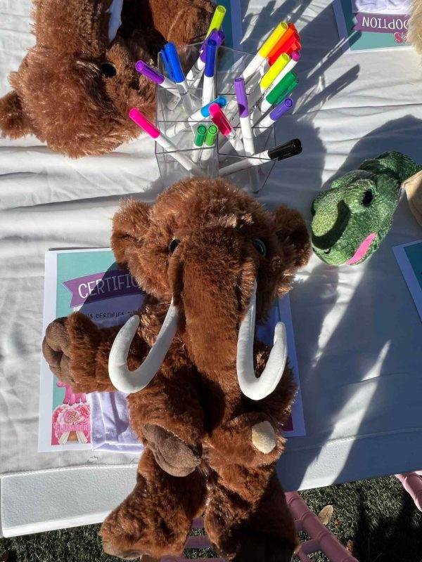 A stuffed toy mammoth holding a colorful bouquet of markers at a Build A Bear party with certificates on the table.
