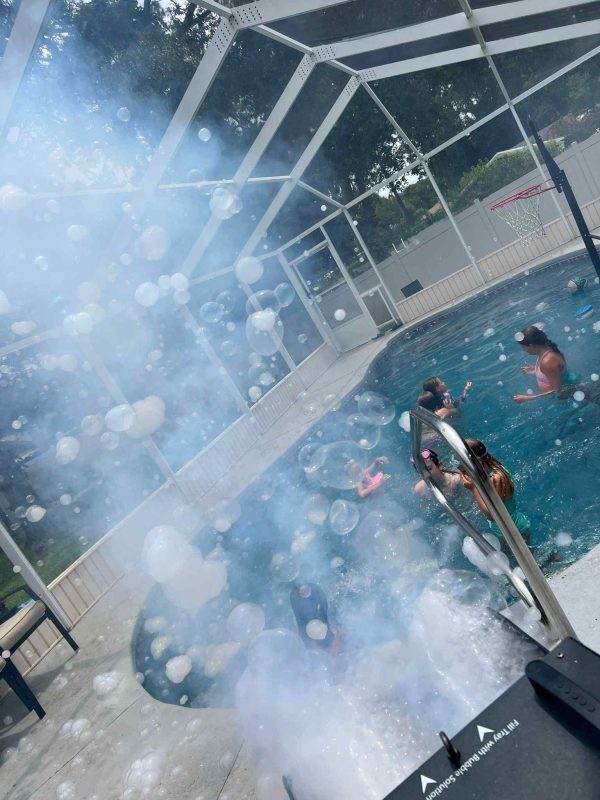 A group of people in a pool at a lively party with Frogger F4 Bubble Fogger Rental coming out of it.