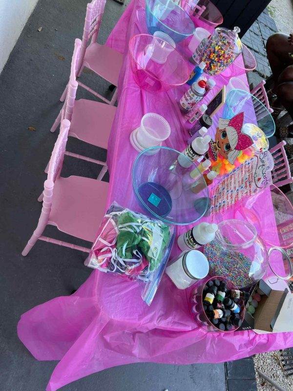 A children's party table covered with a pink tablecloth, displaying candy jars, bowls of sweets, and Winter Haven party favors.