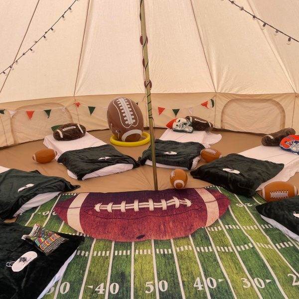 Inside a tent decorated with football-themed bedding and accessories for event planning, including a large rug resembling a football field and helmets.