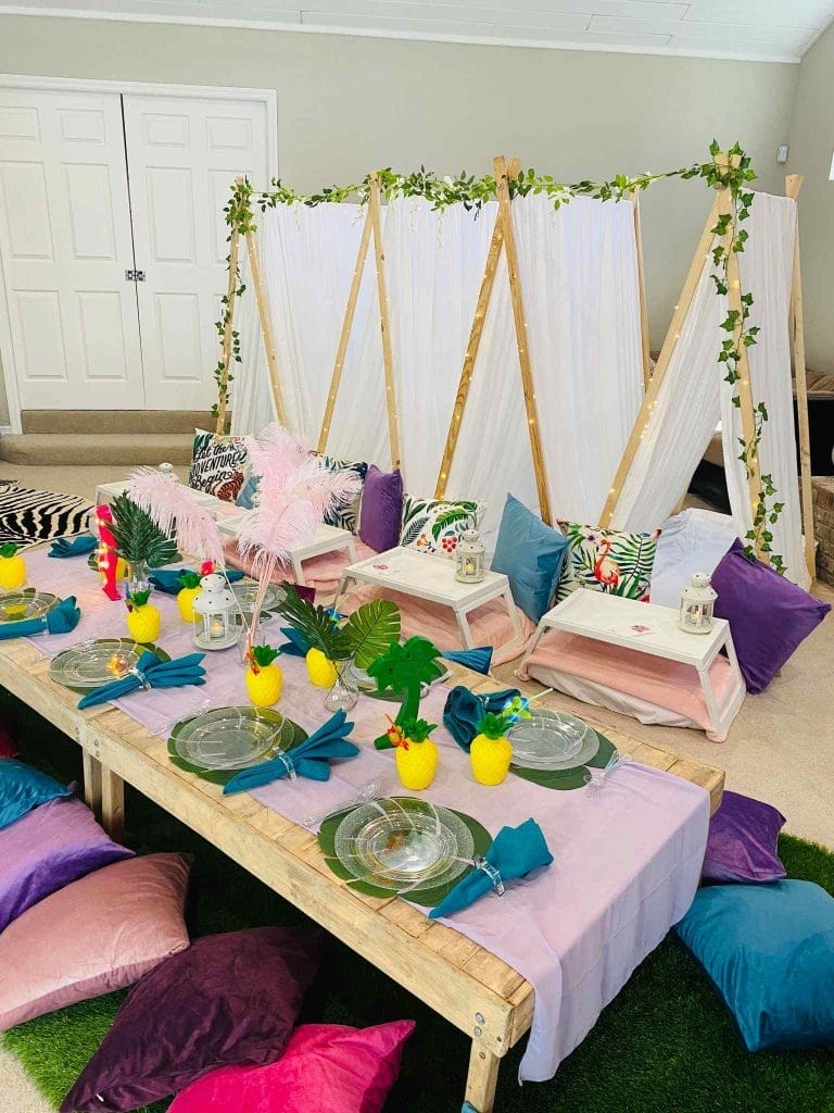 Indoor tropical-themed slumber party setup in Tampa with a low wooden table, colorful cushions, and decorative elements like pineapples and flamingos.