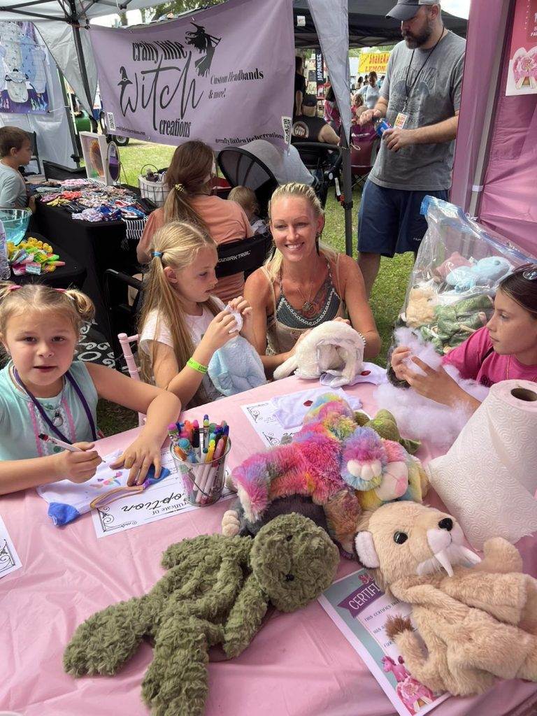 A group of women and children sitting at a table inside a Bell Tent with stuffed animals.