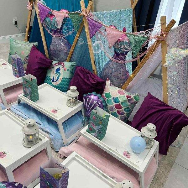 Children's party setup with a mermaid theme, featuring decorated sleepover tents, cushions, and small tables.