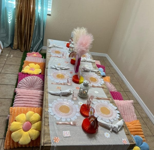 A children's slumber party setup with a decorated table, colorful floor cushions resembling flowers, and tea sets placed on the table.