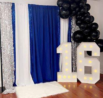 Decorated party corner with blue and silver curtains, a cluster of black balloons, and large white 4FT Marquee Light Up Letters Rental.