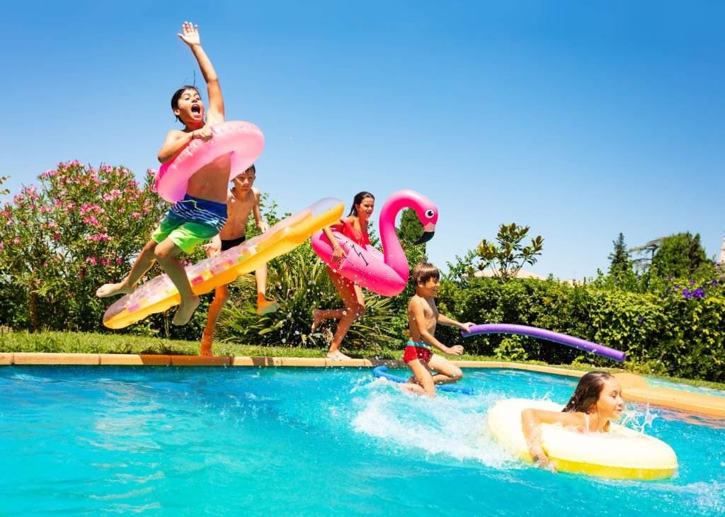 Children playing joyfully in a pool with inflatable floats on a sunny day, near luxury teepees.