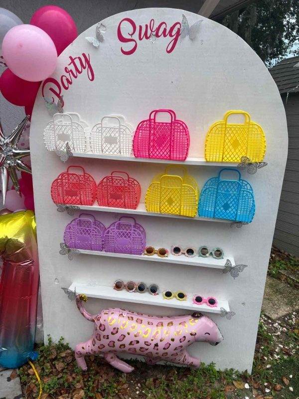 Display board with colorful purses and sunglasses at a party featuring a pink decorated pig sculpture at the bottom, perfectly matching the event planning theme.