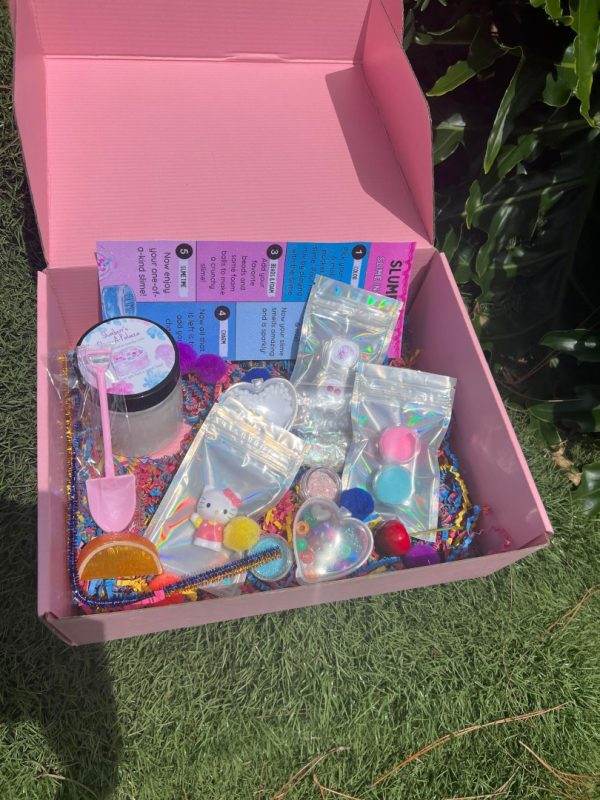 Open Slime party box filled with colorful children's toys and accessories, including beads and hairbands, on a grassy background.