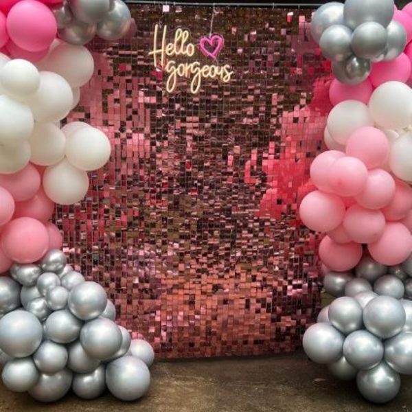 A photo of a party themes wall decorated with pink and silver balloons, and a neon sign that reads "hello gorgeous" in cursive, with a heart shape.