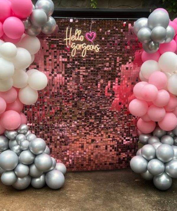 A photo of a party themes wall decorated with pink and silver balloons, and a neon sign that reads "hello gorgeous" in cursive, with a heart shape.
