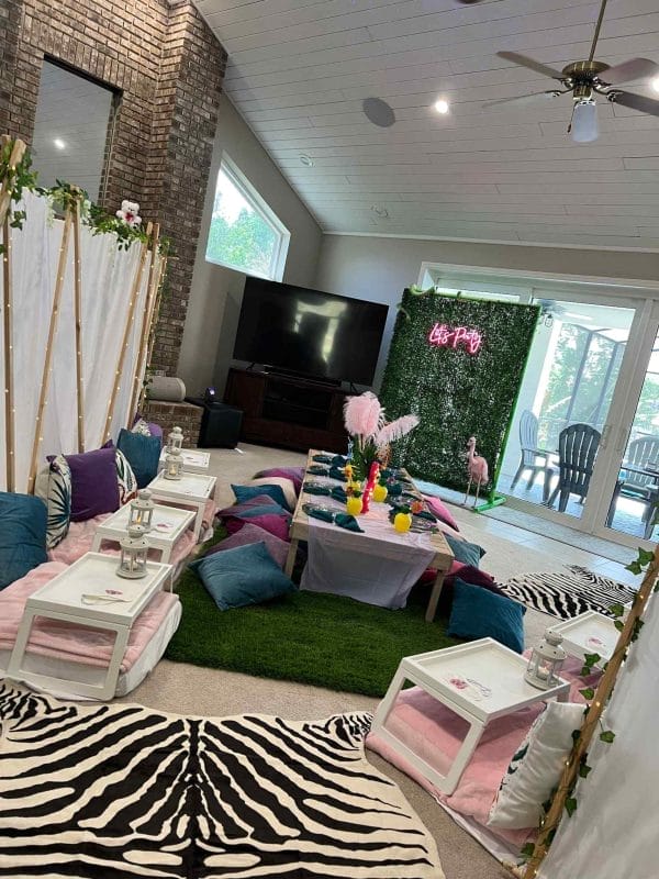 A vibrant living room decorated for the ultimate sleepover, featuring a low seating arrangement with colorful cushions, a floral backdrop, and a zebra print rug.