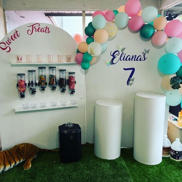 A candy bar setup at a sleepover birthday party with a sign reading "sweet treats" and "liana's 7," decorated with balloons and jars of candy. A toy tiger is on the