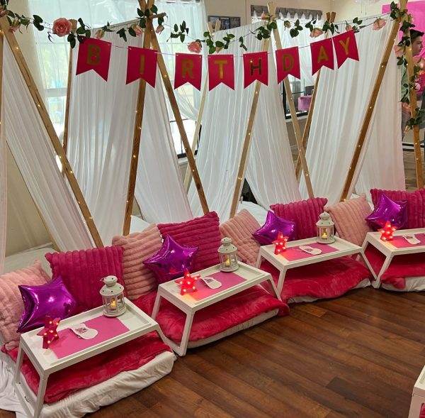 Indoor birthday party themes setup featuring teepee tents with pink cushions and small tables, decorated with a "birthday" banner and star-shaped balloons.