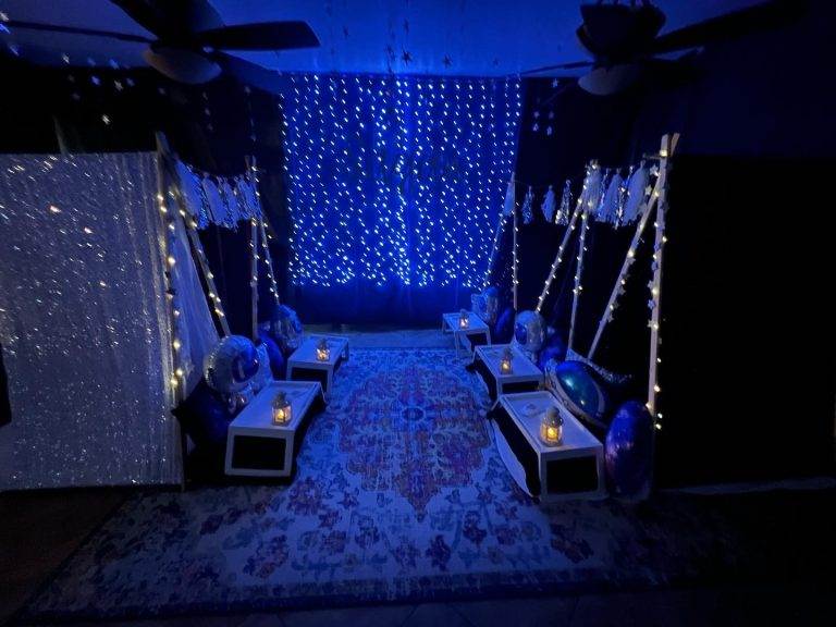 A dimly lit room decorated with blue fairy lights, hanging crystals, and display boxes, creating a serene ambience for party themes.