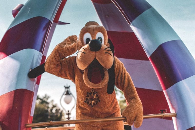 A person in a Pluto costume waving from behind a red and white striped parade float in Orlando.
