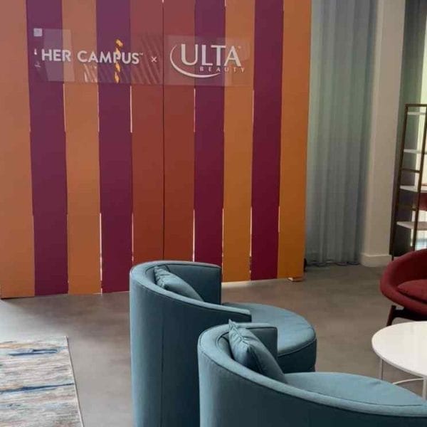 Colorful striped partition with "her campus" and "ulta" logos in a modern lounge area at a corporate event, featuring blue chairs and a decorative rug.