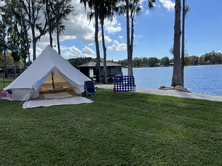 A white bell tent on the grass next to a lake.