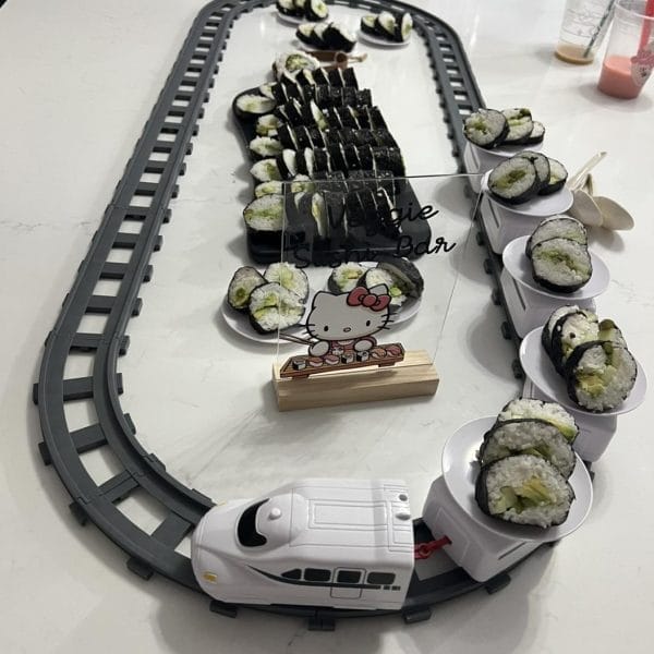 A Sushi Train Rental setup with a variety of sushi rolls placed on a toy train track, featuring a train-shaped serving dish.