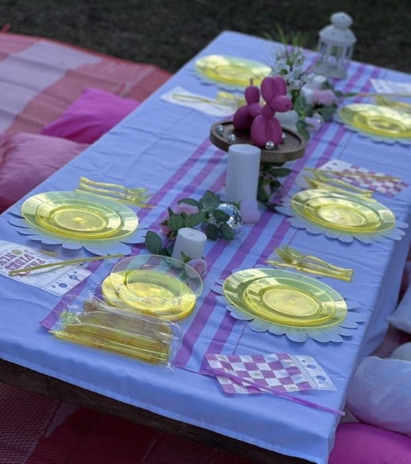 A picnic table set up with pink and yellow plates and napkins, perfect for a glamping experience.