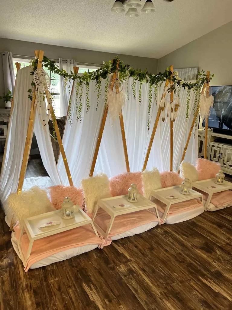 Four enchanting teepees adorned with white drapes and floral decorations, set up with fur rugs and pink pillows, displaying a cozy sleepover setup.