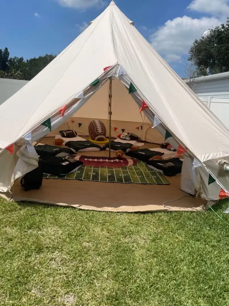 White canvas tent set up outdoors in Central Florida with an interior decorated in a football theme, including a rug designed as a football field and various themed cushions.