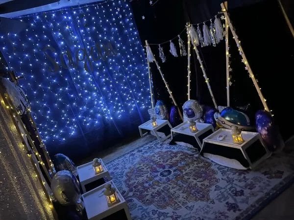 Dark-themed sensory room decorated with twinkling blue lights, hanging stars, and space-themed cushions on swings and an enchanting teepee.